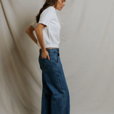 side view of woman in white top and denim on draped background 