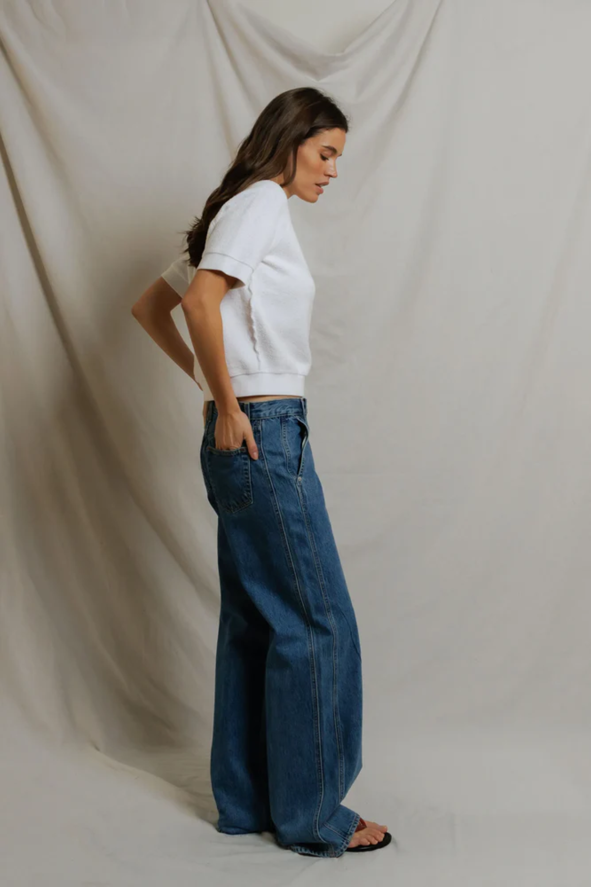 side view of woman in white top and denim on draped background 