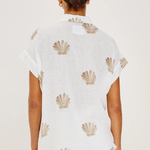 Person wearing a white top with shell patterns on a plain background