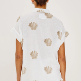 Person wearing a white top with shell patterns on a plain background