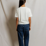 Person wearing a white shirt and blue jeans standing against a plain background