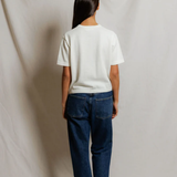 Person wearing a white shirt and blue jeans standing against a plain background