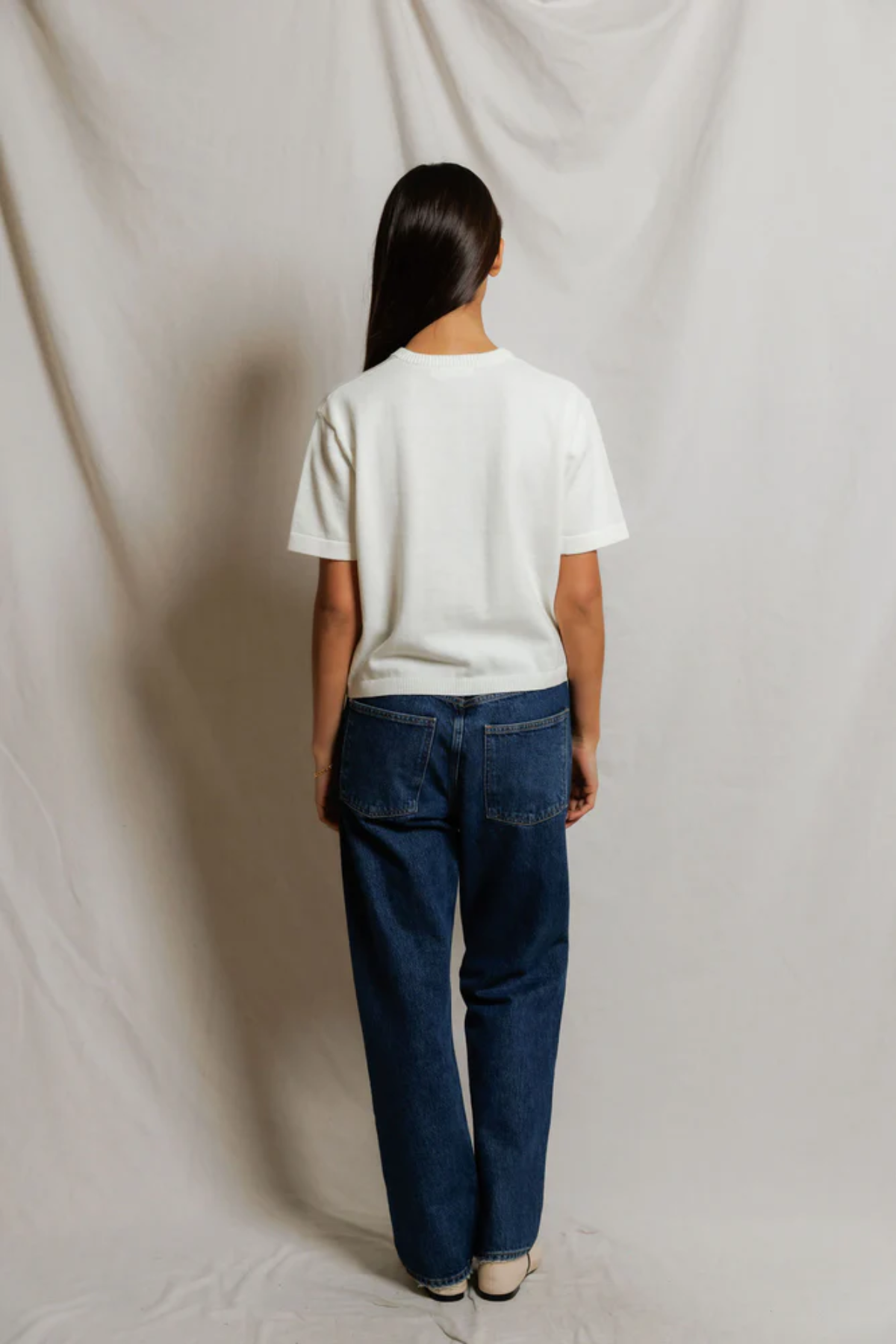 Person wearing a white shirt and blue jeans standing against a plain background
