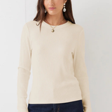 A woman modeling a cream ribbed long-sleeve knit top with dark blue jeans, standing against a plain white background.
