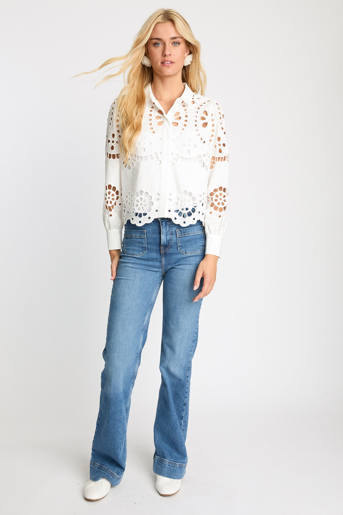 Woman wearing a white lace blouse and blue jeans on a white background
