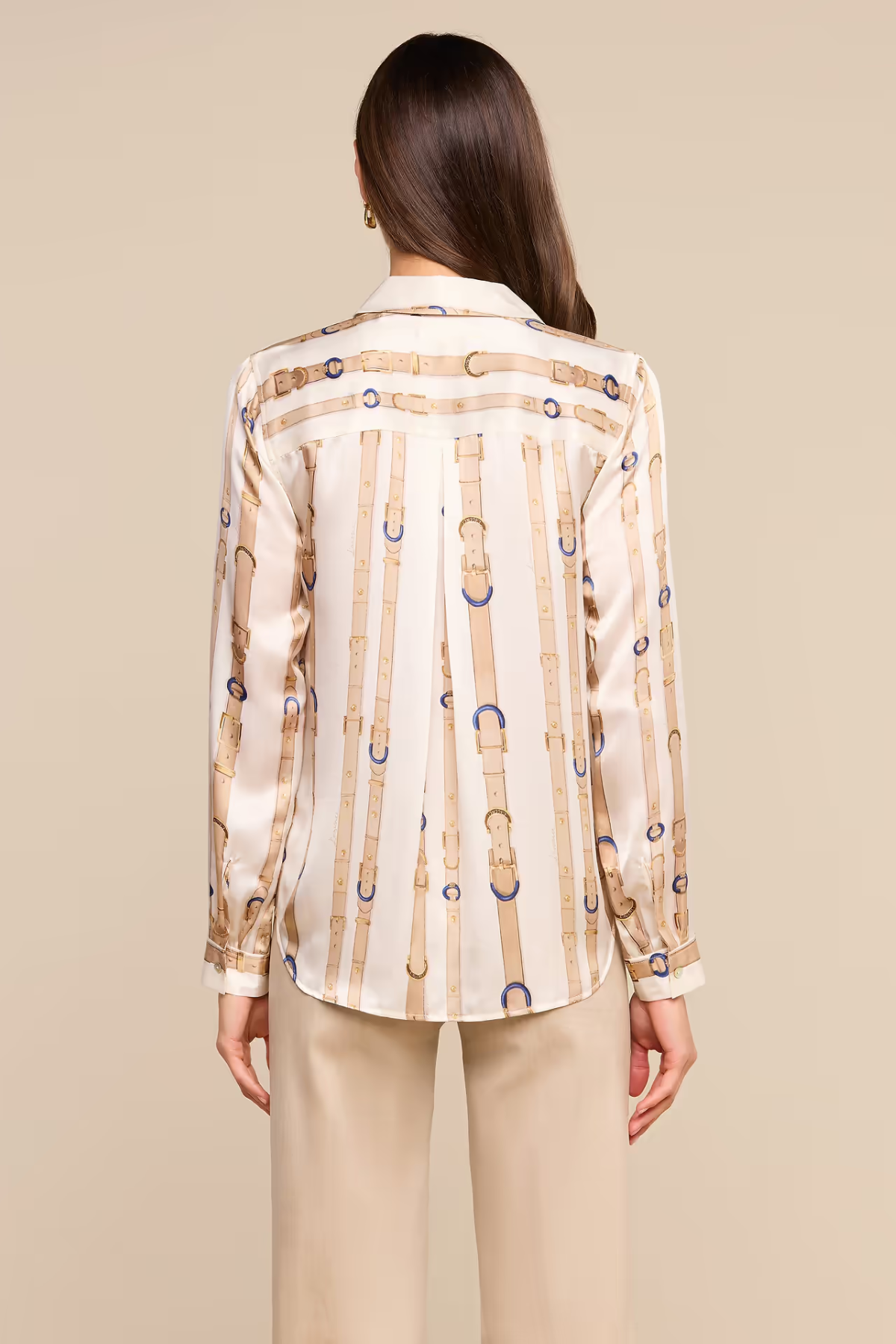 A woman shown from the back wearing a cream satin shirt with vertical gold and blue chain-link patterns, paired with beige trousers, against a solid beige background.