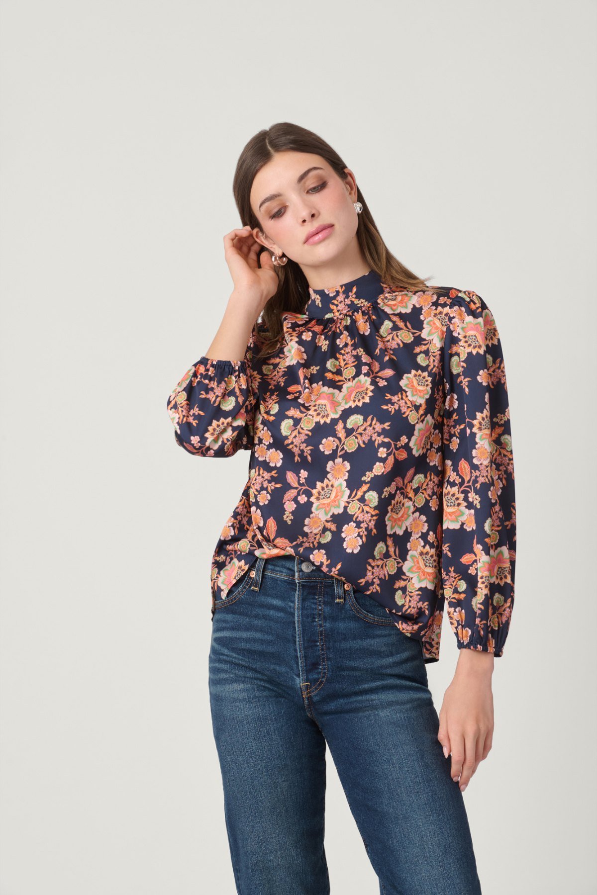 Woman wearing a floral blouse and blue jeans on a light gray background