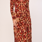 A long-sleeve midi dress with a gathered waist and an all-over abstract pattern in rust red, orange, beige, and brown, shown on a model against a plain light background.