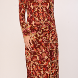 A long-sleeve midi dress with a gathered waist and an all-over abstract pattern in rust red, orange, beige, and brown, shown on a model against a plain light background.