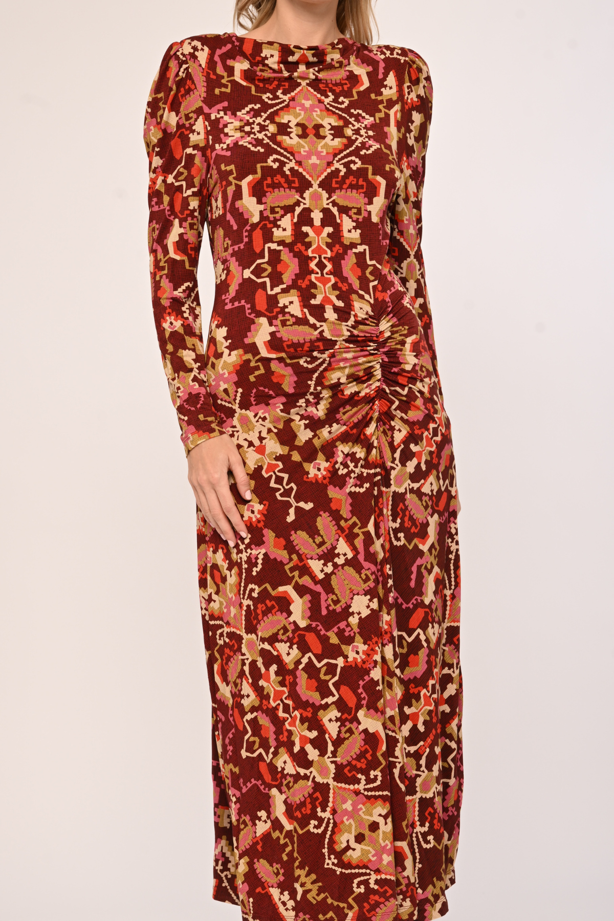 A long-sleeve midi dress with a gathered waist and an all-over abstract pattern in rust red, orange, beige, and brown, shown on a model against a plain light background.