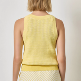 Woman wearing a yellow sleeveless top and striped skirt on a plain background