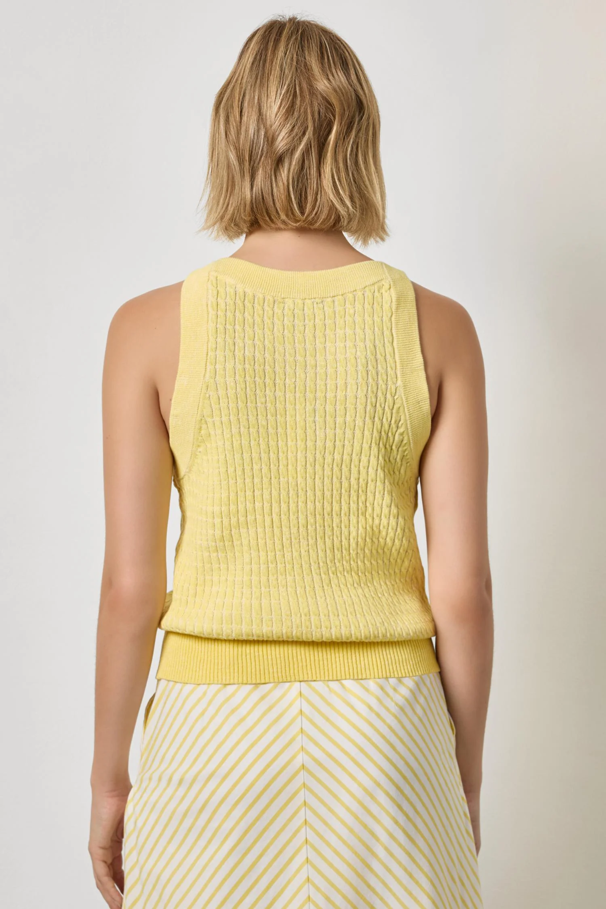 Woman wearing a yellow sleeveless top and striped skirt on a plain background