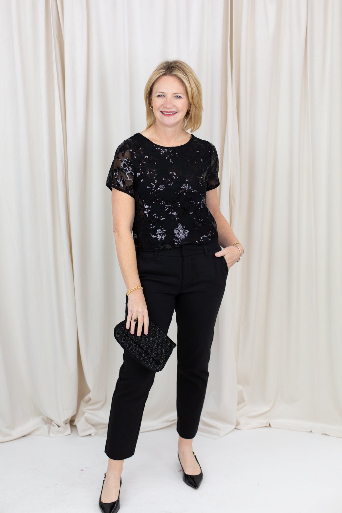 Woman wearing black chino trousers with a front hem split, styled with heels.