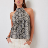 A woman modeling a sleeveless high-neck top with a gray and black snakeskin pattern, paired with cream-colored pants, standing against a plain light gray wall.
