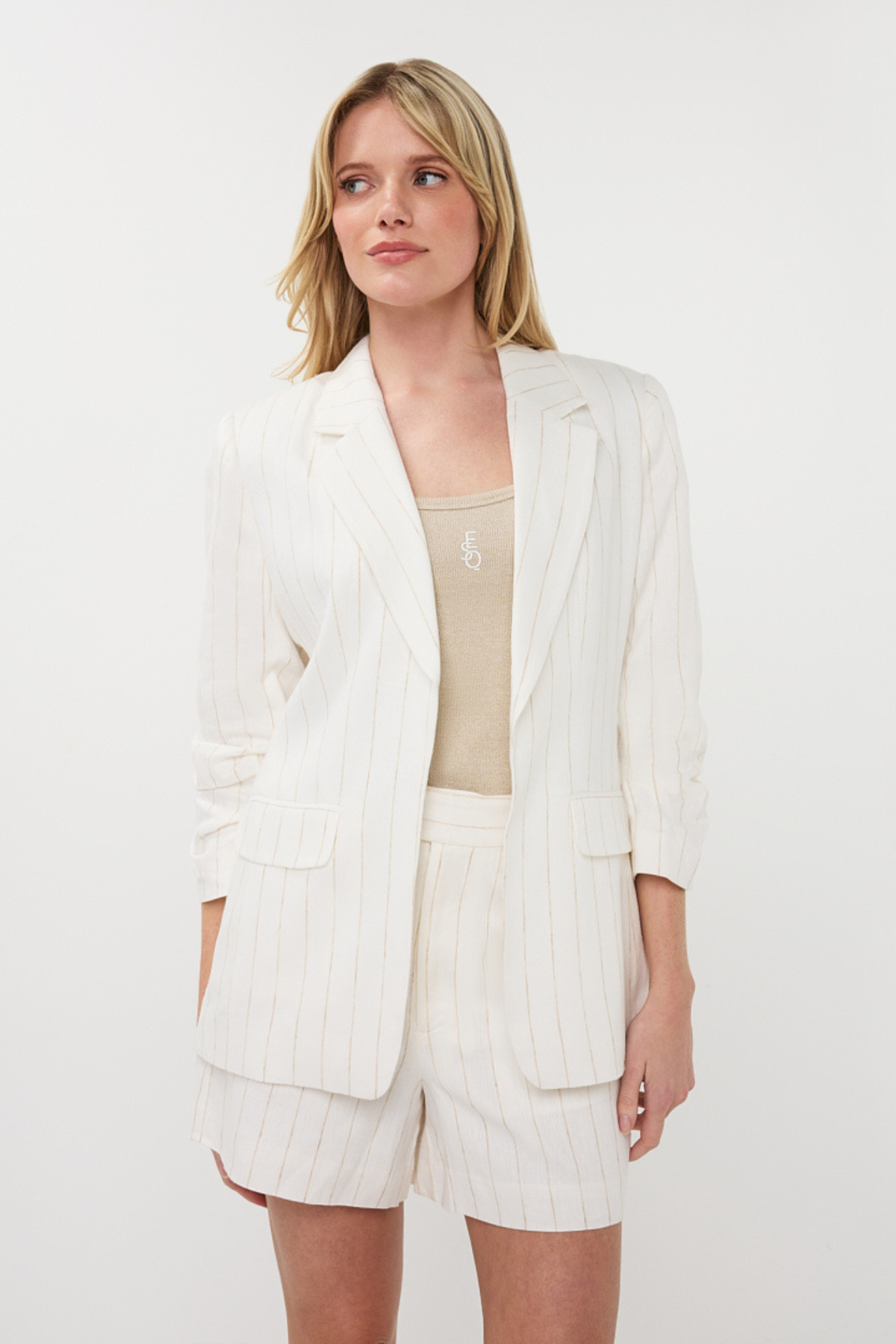 Woman wearing a white blazer and shorts set on a plain background