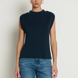 Woman wearing a navy sleeveless top and blue jeans against a white background