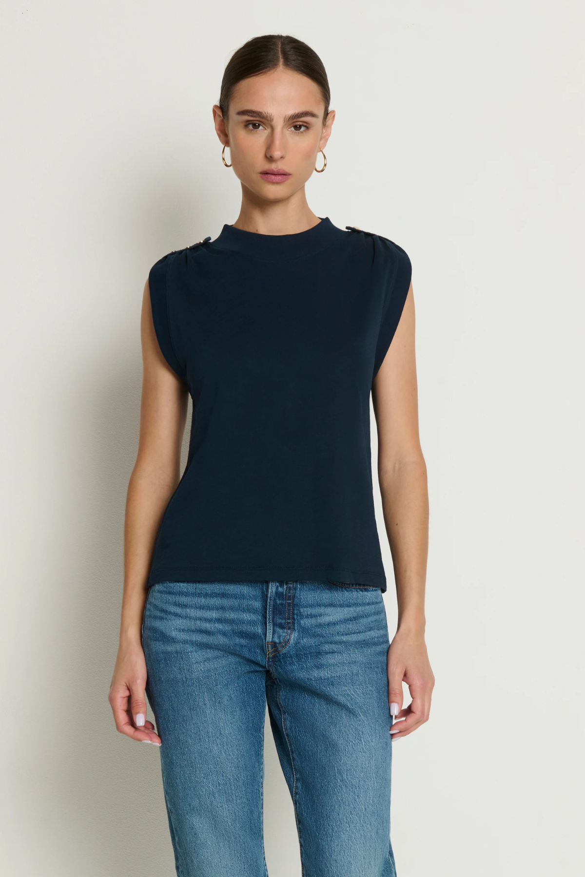 Woman wearing a navy sleeveless top and blue jeans against a white background