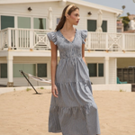 Woman in a blue striped dress standing on a sandy beach with a house in the background