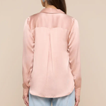 Woman wearing a light pink blouse and light blue jeans against a beige background