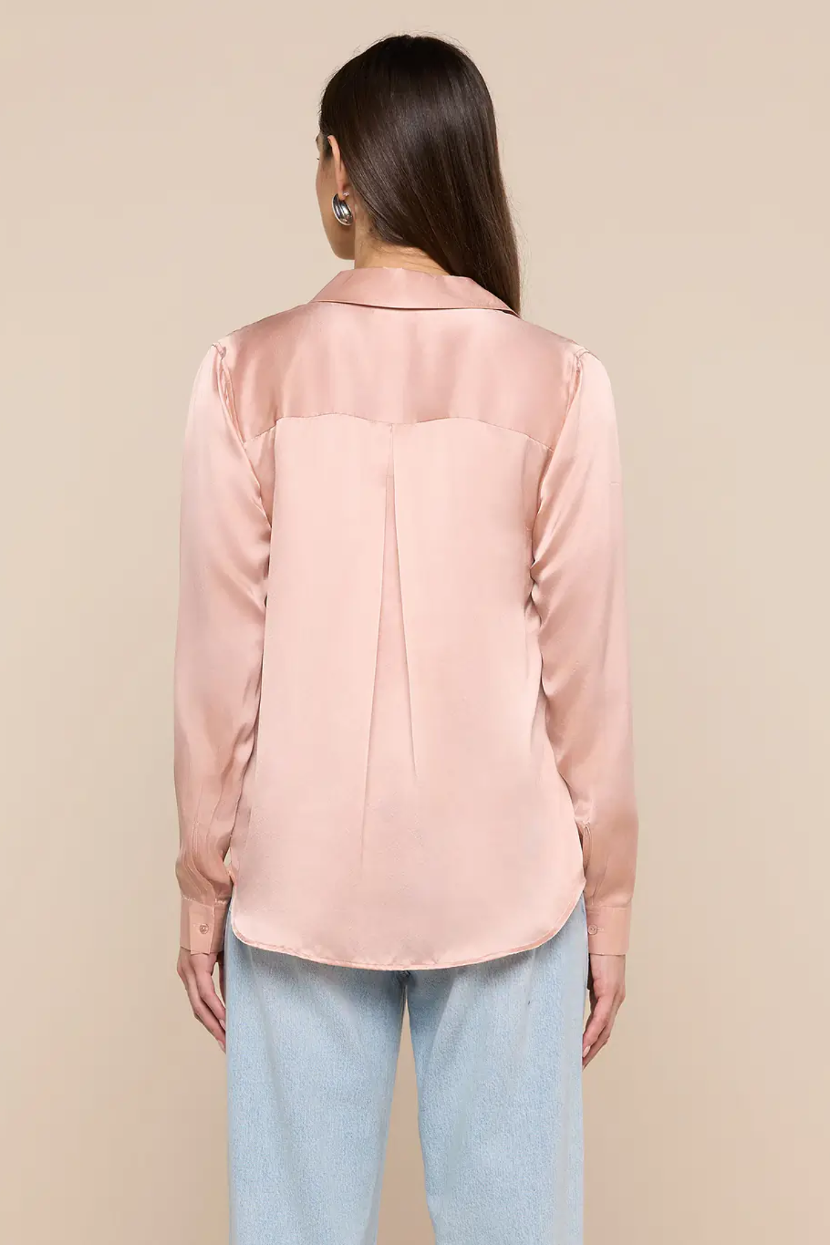 Woman wearing a light pink blouse and light blue jeans against a beige background
