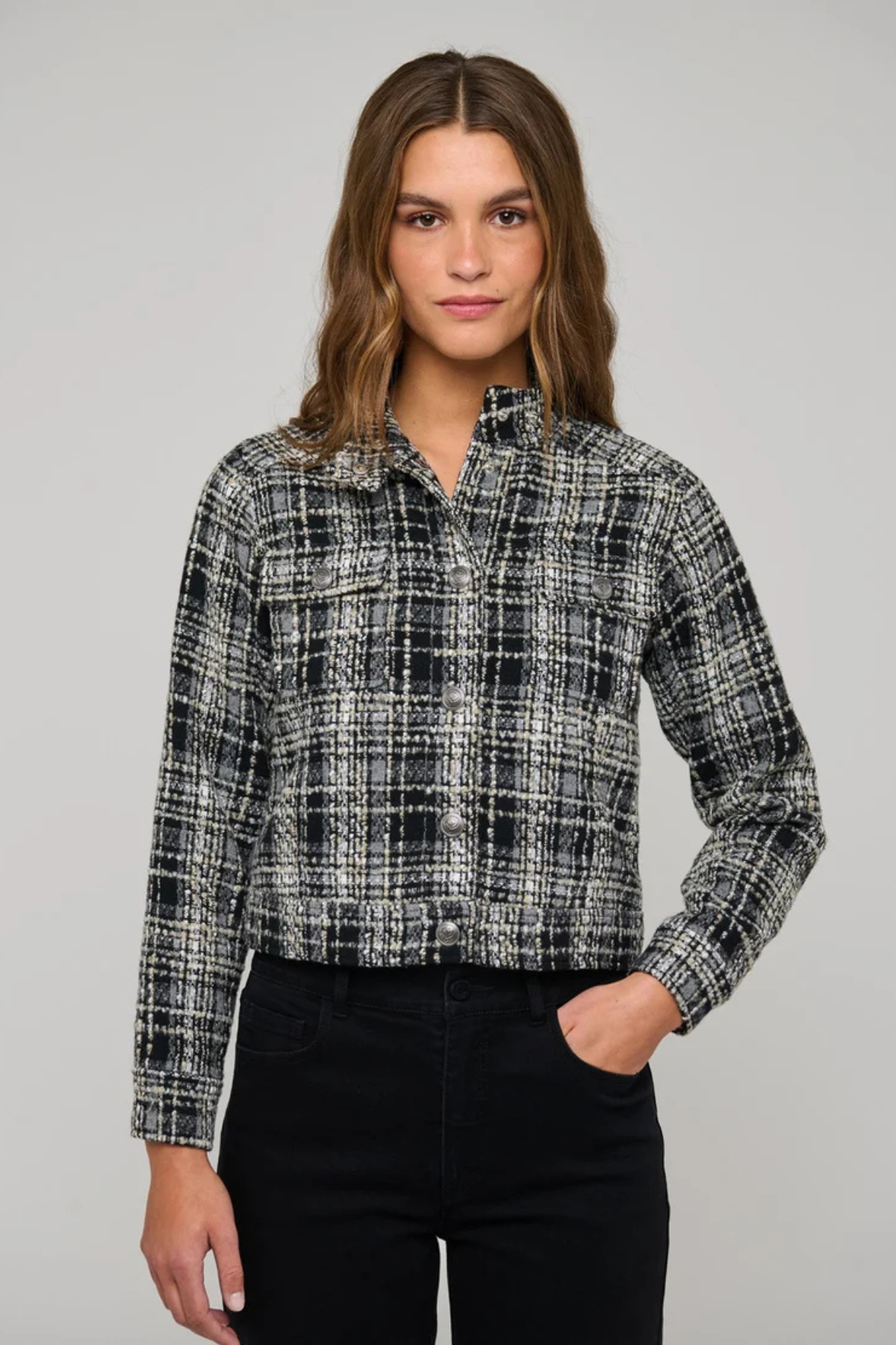 A woman modeling a black and white plaid tweed button-up shirt jacket with black pants, photographed against a solid light gray studio background.