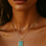 Close-up of a person wearing a gold necklace with a turquoise pendant.
