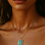 Close-up of a person wearing a gold necklace with a turquoise pendant.