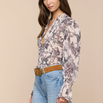 Woman wearing a floral blouse and blue jeans against a beige background