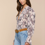 Woman wearing a floral blouse and blue jeans against a beige background
