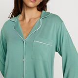 Woman wearing a teal nightshirt with white piping on a plain background