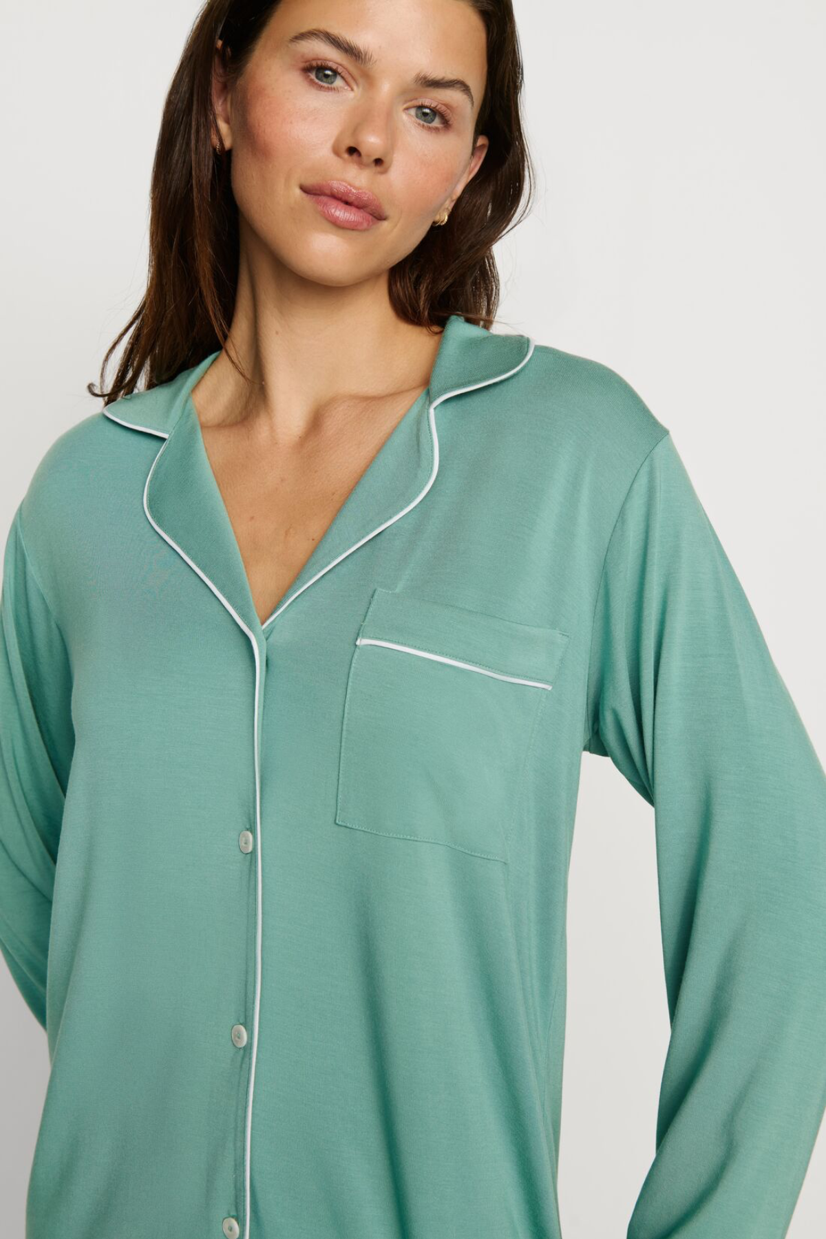 Woman wearing a teal nightshirt with white piping on a plain background