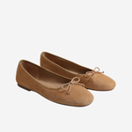 A pair of tan suede ballet flats with small bow details on the toes, shown against a plain light gray background.