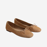 A pair of tan suede ballet flats with small bow details on the toes, shown against a plain light gray background.