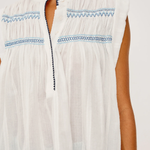 White sleeveless top with blue embroidery on a white background