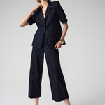 Woman wearing a navy blue suit with wide-leg pants on a light gray background