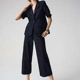 Woman wearing a navy blue suit with wide-leg pants on a light gray background