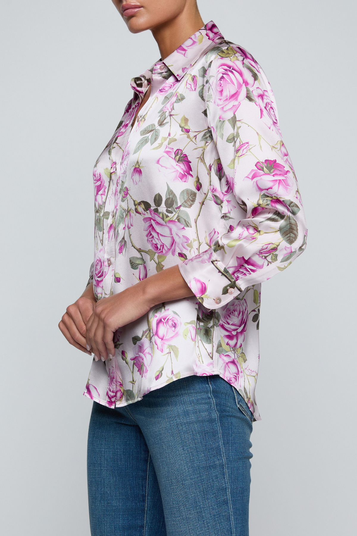 Model wearing rose print blouse with jeans on white background.