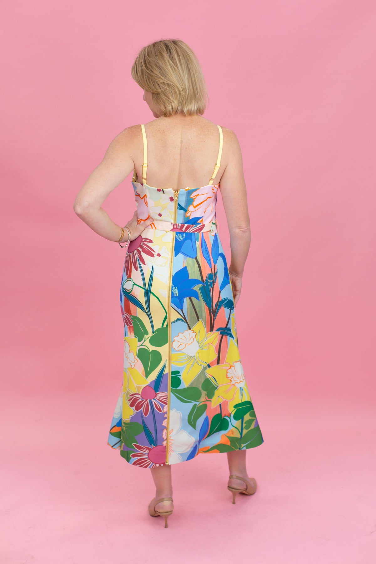Woman wearing a colorful floral dress against a pink background