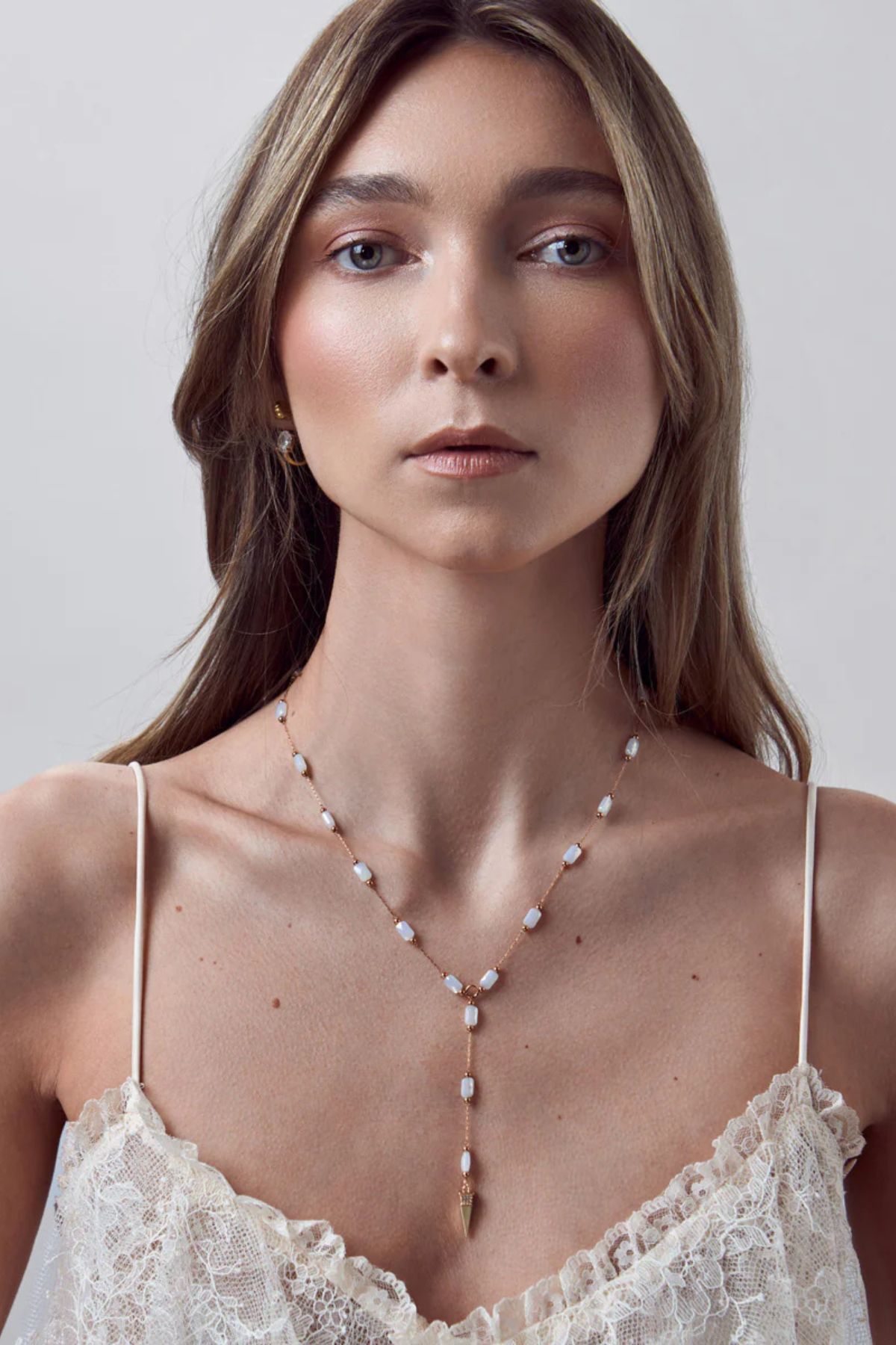Woman wearing a delicate necklace with a plain background