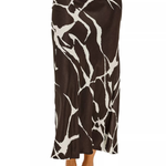 A woman wearing a brown and white abstract animal-print maxi skirt with white strappy high-heeled sandals, shown from the waist down on a white background.
