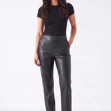 A woman modeling a pair of black faux-leather straight-leg pants, paired with a black short-sleeve t-shirt and black pointed-toe mule heels, against a plain white studio background.