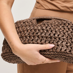 Brown woven clutch held by a person wearing a brown outfit on a light background