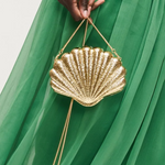 Gold shell-shaped handbag held by a hand against a green fabric background