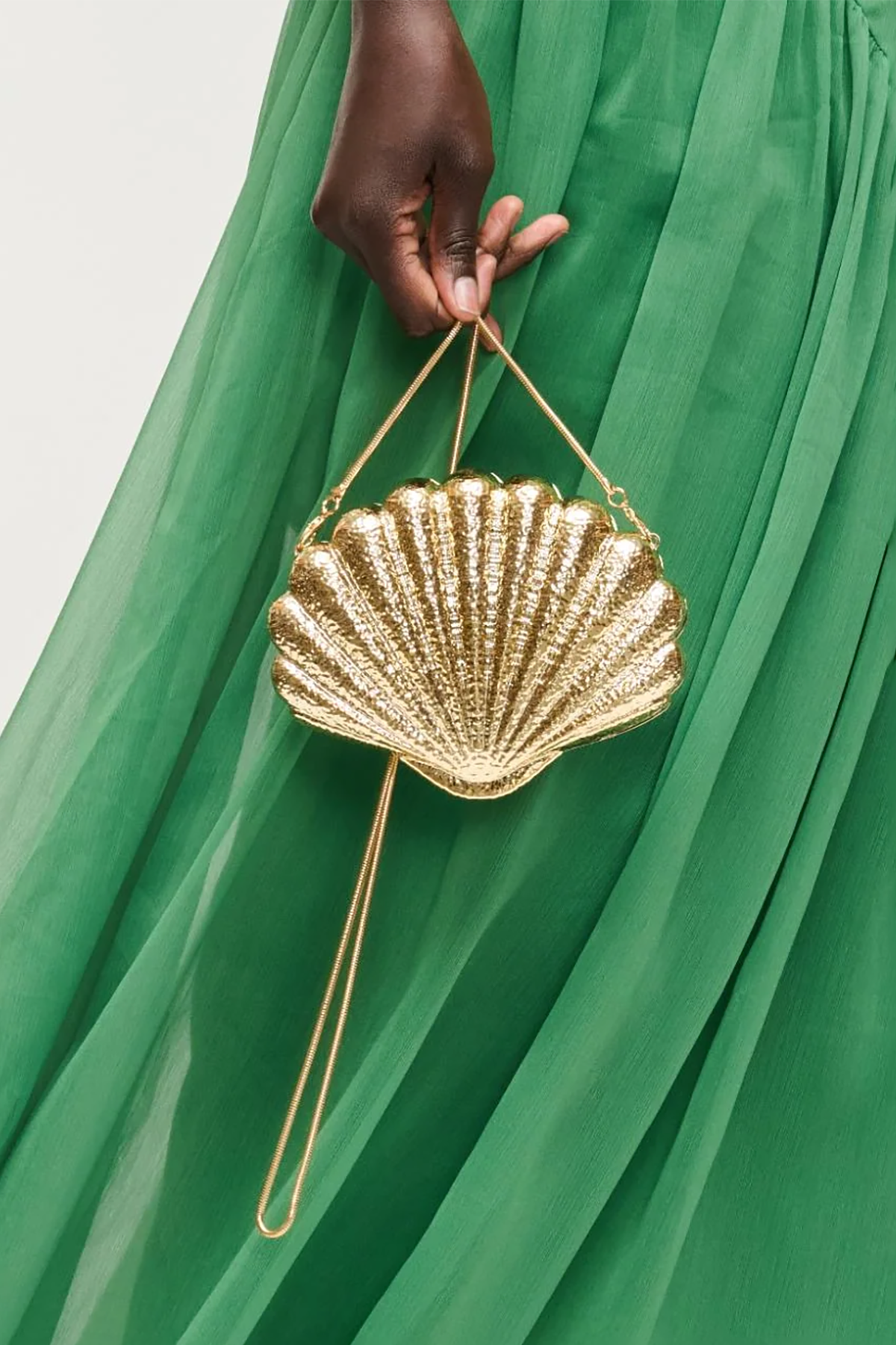 Gold shell-shaped handbag held by a hand against a green fabric background