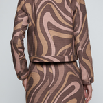 A model shown from the back wearing a matching cropped jacket and skirt set with a brown, beige, and dusty pink wavy abstract pattern.
