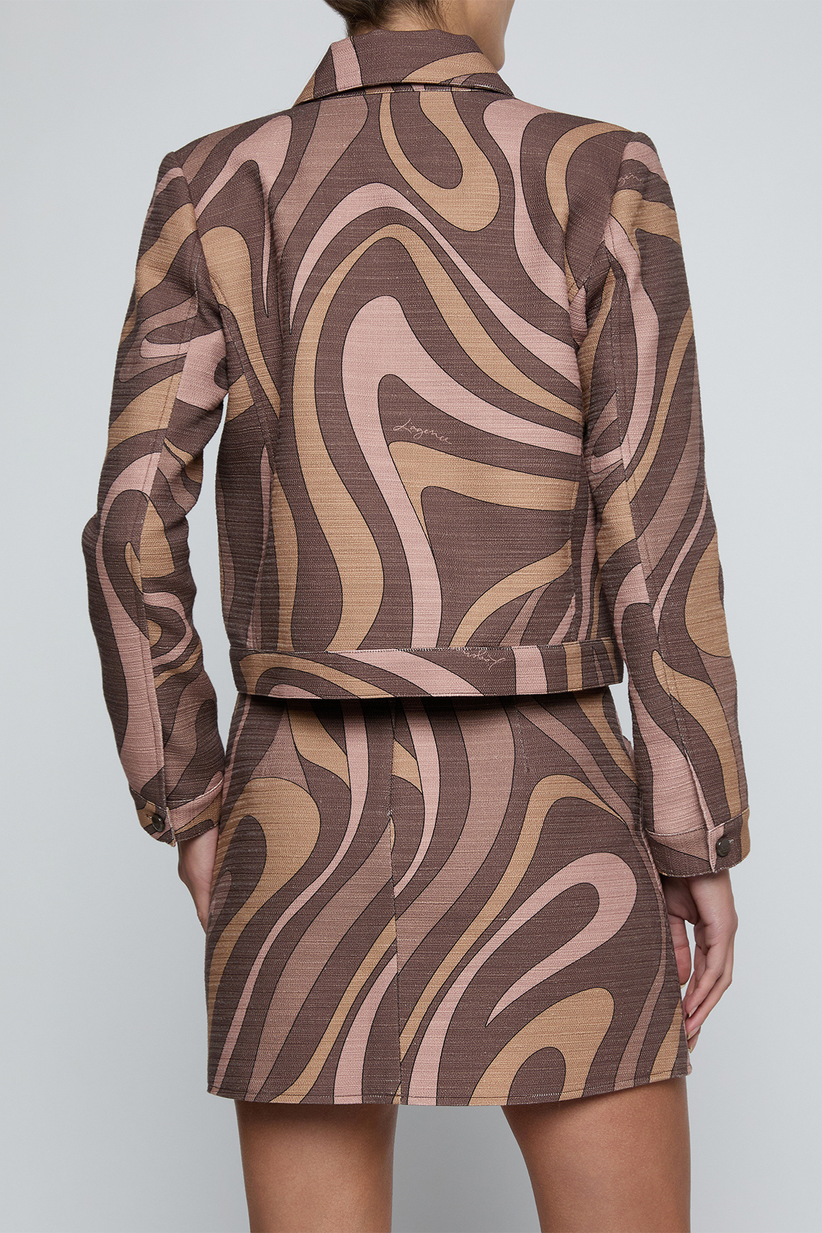 A model shown from the back wearing a matching cropped jacket and skirt set with a brown, beige, and dusty pink wavy abstract pattern.
