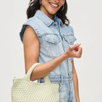 Woman holding a light green woven handbag against a plain background