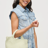 Woman holding a light green woven handbag against a plain background