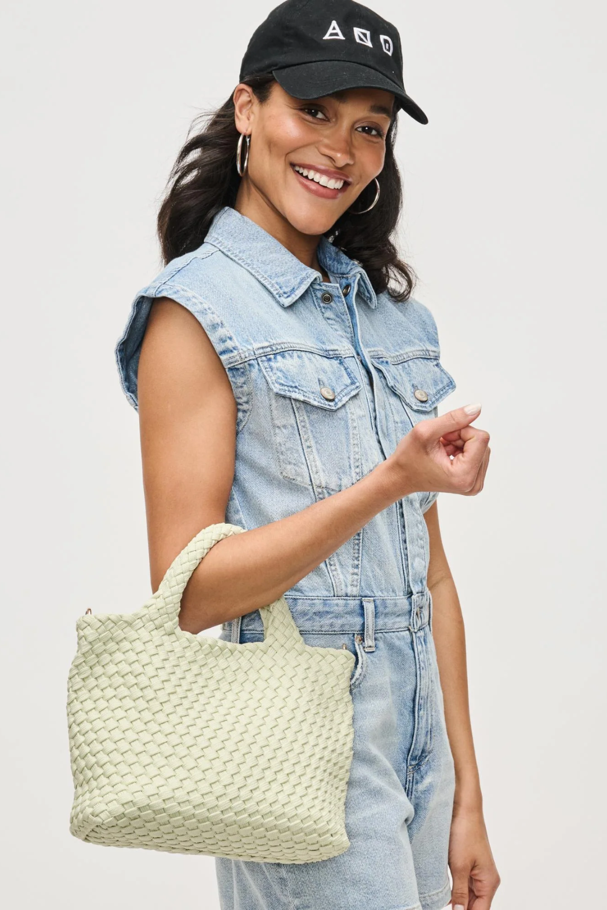 Woman holding a light green woven handbag against a plain background