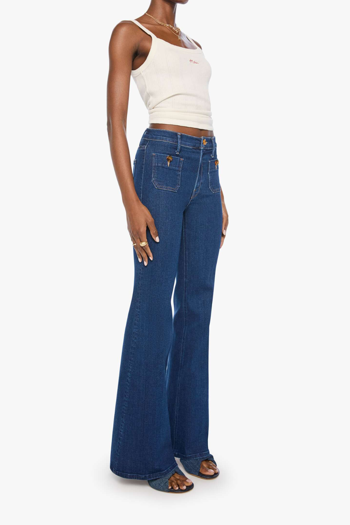 A model wearing a pair of high-waisted, wide-leg blue denim jeans with a cream ribbed tank top, shown from a side profile against a light gray background.